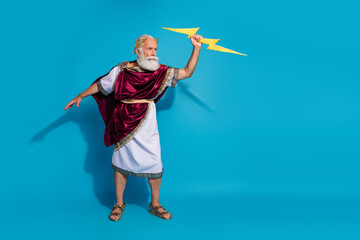 Full length photo of attractive old man punish hit lightning dressed greek god emperor actor costume isolated on blue color background
