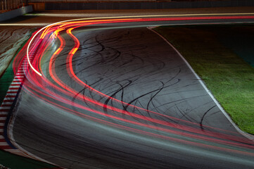 Long exposure night photography that shows the traces of light left by the racing cars as they pass through the curve. There is a line that shows an overtaking