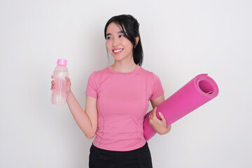 A young woman smiling happy while holding a drink bottle and yoga mat