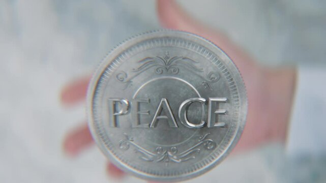 A hand flips a coin marked War and Peace, spinning toward the camera in slow motion
