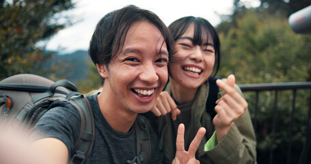 Fototapeta premium Peace sign, selfie and smile with couple in nature for holiday, travel or vacation on mountains of Japan. Adventure, hiking and photograph with Japanese people outdoor on Mount Takao for memory
