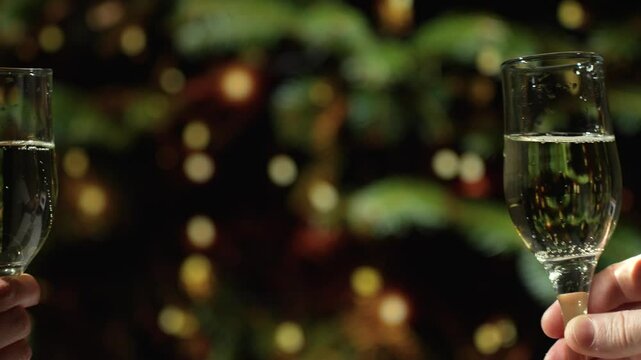 Two glasses of sparkling champagne clink together, with Christmas tree lights on background. A toast with sparkling wine for New Year Celebration
