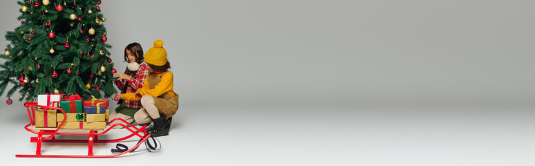 Excited girls arrange colorful presents near an adorned Christmas tree ready for festivities.