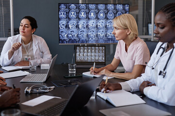 Side view of female radiologist writing notes in notebook interpreting brain images from CT scans...