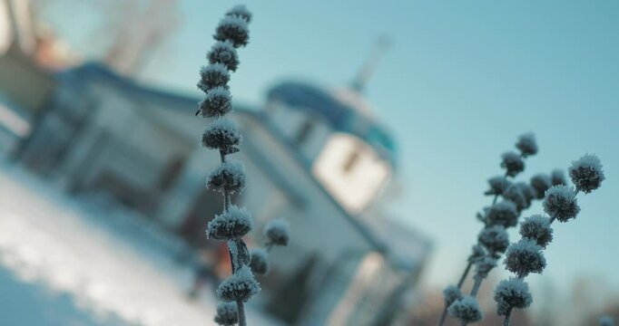 Religion. Bokeh. A dry grass covered with frost against the background of a man passing by a small Orthodox church. Rotation of the camera. Siberia.