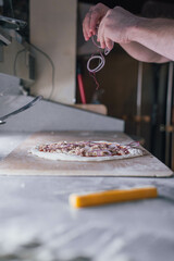 A close-up of hands sprinkling ingredients onto a pizza base showcases the attention to detail in creating authentic pizza.