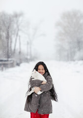 A girl stands outside in the snowfall and holds her white cat in her arms