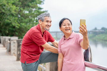 Naklejka premium healthy asian senior couple exercising and relaxing on running walkway by the river in the city,elderly lifestyle,wellness,wellbeing