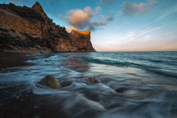 The rock rises above the blue sea at sunset or sunrise