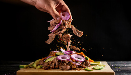 Close up of meat and vegetables falling from a hand gripping a loaded döner kebab against a dark background