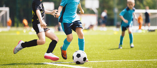 Fototapeta premium Junior football competition between players running and kicking soccer ball. Young boys playing a soccer game. Training and football match between youth soccer teams. Final game of football tournament