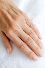Fototapeta premium A close-up view of a mature woman's hand resting gracefully on a white textured surface, symbolizing elegance.