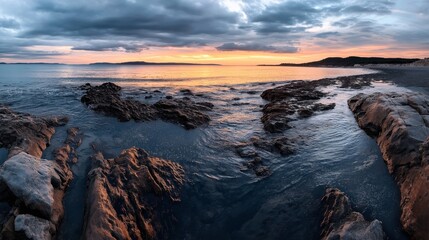 Obraz premium Rocky coastline at sunset with dramatic clouds and vibrant sky reflecting on the ocean water