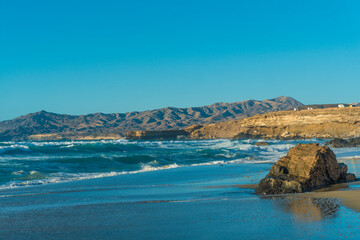 Fototapeta premium A wide shot of La Pared beach on the island of Fuerteventura, Canary Islands, Spain. The photo showcases the beautiful blue sky, the turquoise ocean with gentle waves, and the sandy beach with seaweed