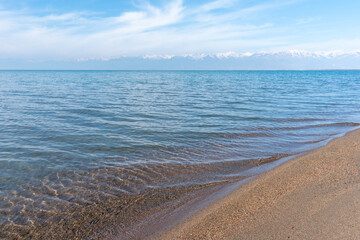 Issyk-Kul's crystal clear waters with snowy mountains background during beautiful sunny weather in late November.