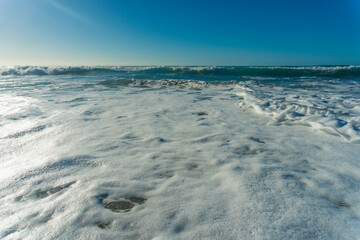 A wide shot of La Pared beach on the island of Fuerteventura, Canary Islands, Spain. The photo showcases the beautiful blue sky, the turquoise ocean with gentle waves, and the sandy beach with seaweed