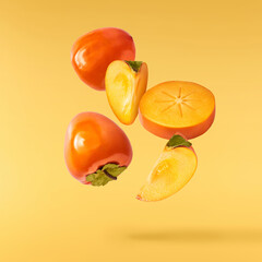 Fresh ripe Persimone fruit falling in the air isolated on yellow background, food levitation or...