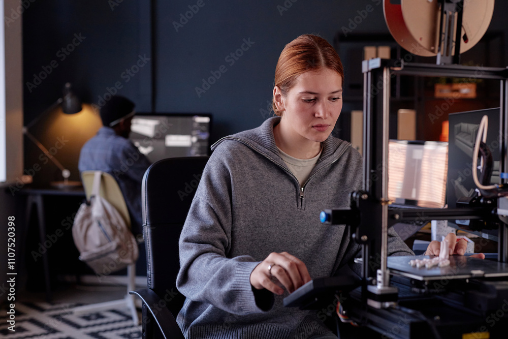 Leinwandbilder Woman sitting at desk working with 3D printer while colleague is in background focusing on his screen showing a busy and tech-savvy environment
