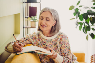 Charming elderly woman enjoying a quiet moment with a journal in autumn light indoors