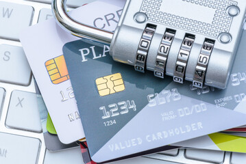 Cybersecurity, online fraud prevention, personal data encryption and protection, credit card security : Several credit cards with a silver combination padlock placed over a computer keyboard.