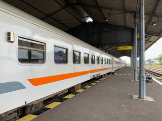 Train at the Railway Station Platform Indonesia, waiting for departure, long white carriage with orange stripe