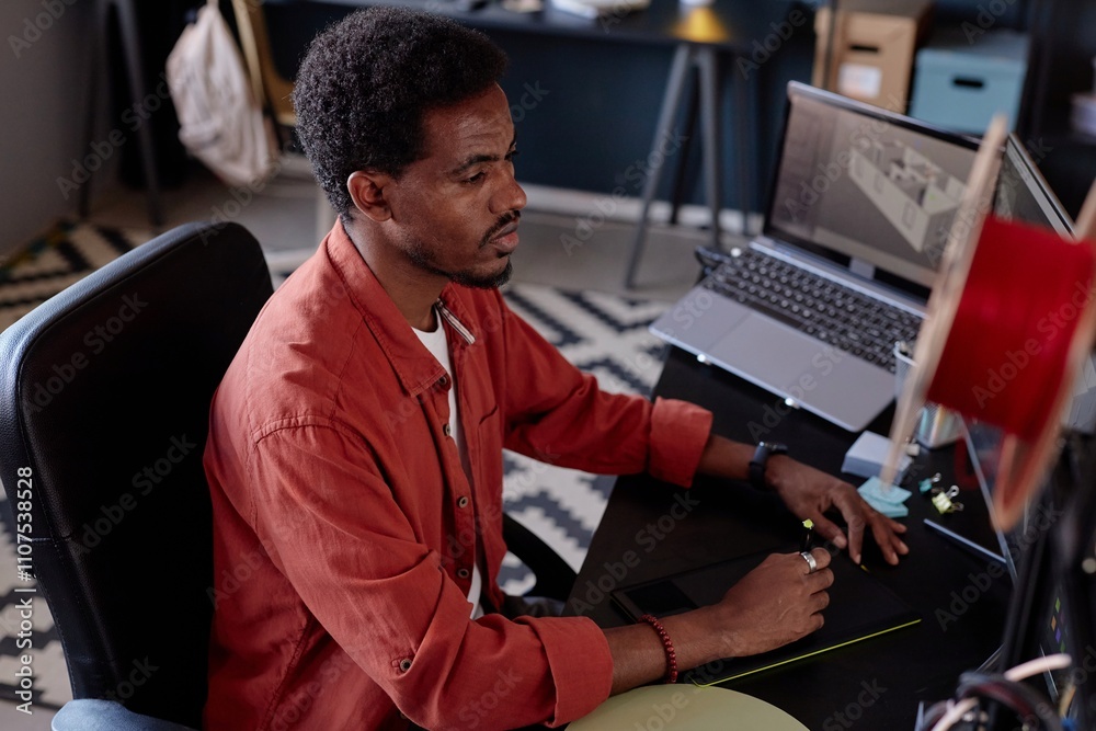 Fototapete Man sitting at a desk with CAD software on screen, creating intricate 3D models for tech project. Surroundings include a modern office space with various tools and gadgets