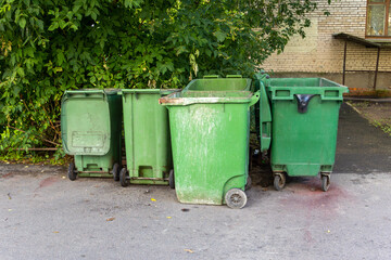 A row of green trash cans are lined up on the street. The trash cans are all different sizes and are placed in a row