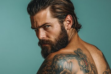 Serious bearded man with tattoos showing his back and turning his head