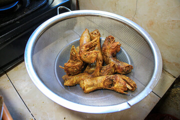 A close-up shot of deep-fried chicken heads in a metal colander. The chickens are golden brown and appear crispy. Deep deep-fried chicken Heads in a Metal Colander.