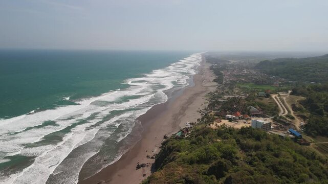 Slow forward moving aerial shot of depok beach with waves slowly washing onto the shore.