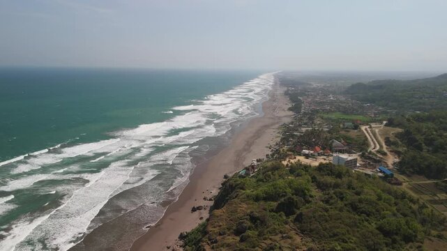 Static aerial shot of depok beach with waves slowly washing onto the shore.