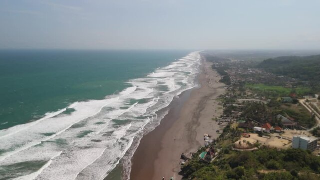 Slow sideways moving aerial shot of depok beach in Yogyakarta, Indonesia, with waves slowly washing onto the shore.