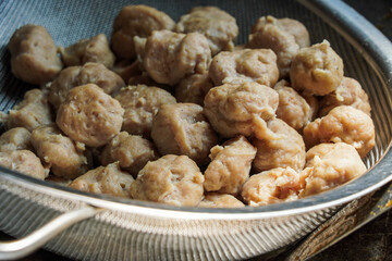 A close-up shot of freshly made meatballs in a metal colander. The meatballs are light brown and appear soft and tender. Close-up of Meatballs in a Metal Colander