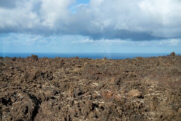 Volcanic landscape meets ocean under cloudy sky.