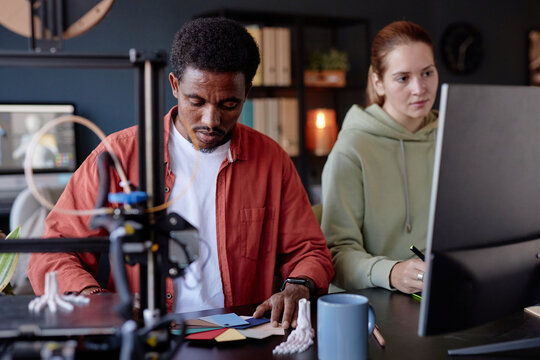 Man and woman working on 3D printing project, focusing on creating model with precision while discussing details. Office setting features modern tools and relaxed atmosphere