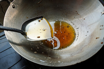 A close-up view of a wok containing used cooking oil and a ladle. Used Cooking Oil in a Wok.