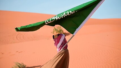 Amidst the golden desert, a Saudi man in traditional attire waves the national Saudi flag celebrating National and Founding Day with pride a stunning symbol of heritage unity, and the Kingdom's legacy