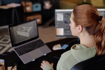 Person sitting at desk and observing design layout on computer screen, focusing attentively....
