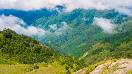 Fototapeta premium Bright clouds hover above a lush mountain landscape under clear blue skies