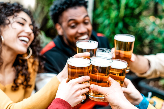 Happy diverse friends toasting and drinking beer glasses at brewery pub garden - Group of young people enjoying happy hour drinking alcohol sitting together at bar dehor - Food and beverage concept