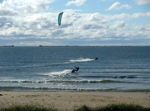View of the sea with a pier in the distance, kiteboarders, beach and dunes in the foreground