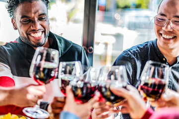 Young multi ethnic people drinking and toasting red wine at lunch party - Happy multiracial friends...