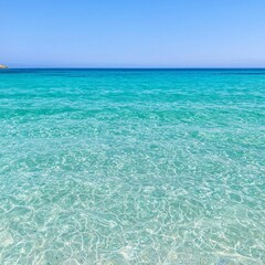 Fototapeta premium Clear turquoise ocean water with a small island in the distance under a clear blue sky.