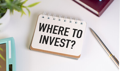 Where to invest text on blank notebook paper on white table with hand holding pencil. Business...