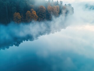 Fototapeta premium A serene landscape featuring fog over a lake, with autumn trees reflecting in calm waters, creating a peaceful and atmospheric scene.