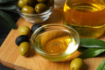 Bowl of fresh olive oil and olives with leaves on the table 