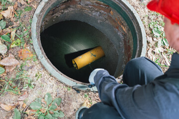 A worker with a flashlight inspects an open sewer manhole. Septic tank maintenance, sewage pumping