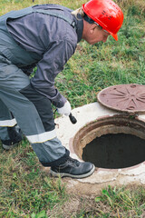 A worker in a helmet with a flashlight inspects an open well. Maintenance of water wells, septic...