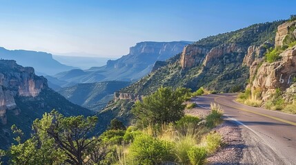 Fototapeta premium Scenic mountain road winding through lush green valleys under a clear blue sky.