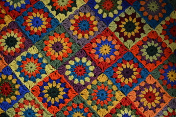 Multicolored crochet plaid made from squares of wool yarn in red, yellow, green, blue and purple colors